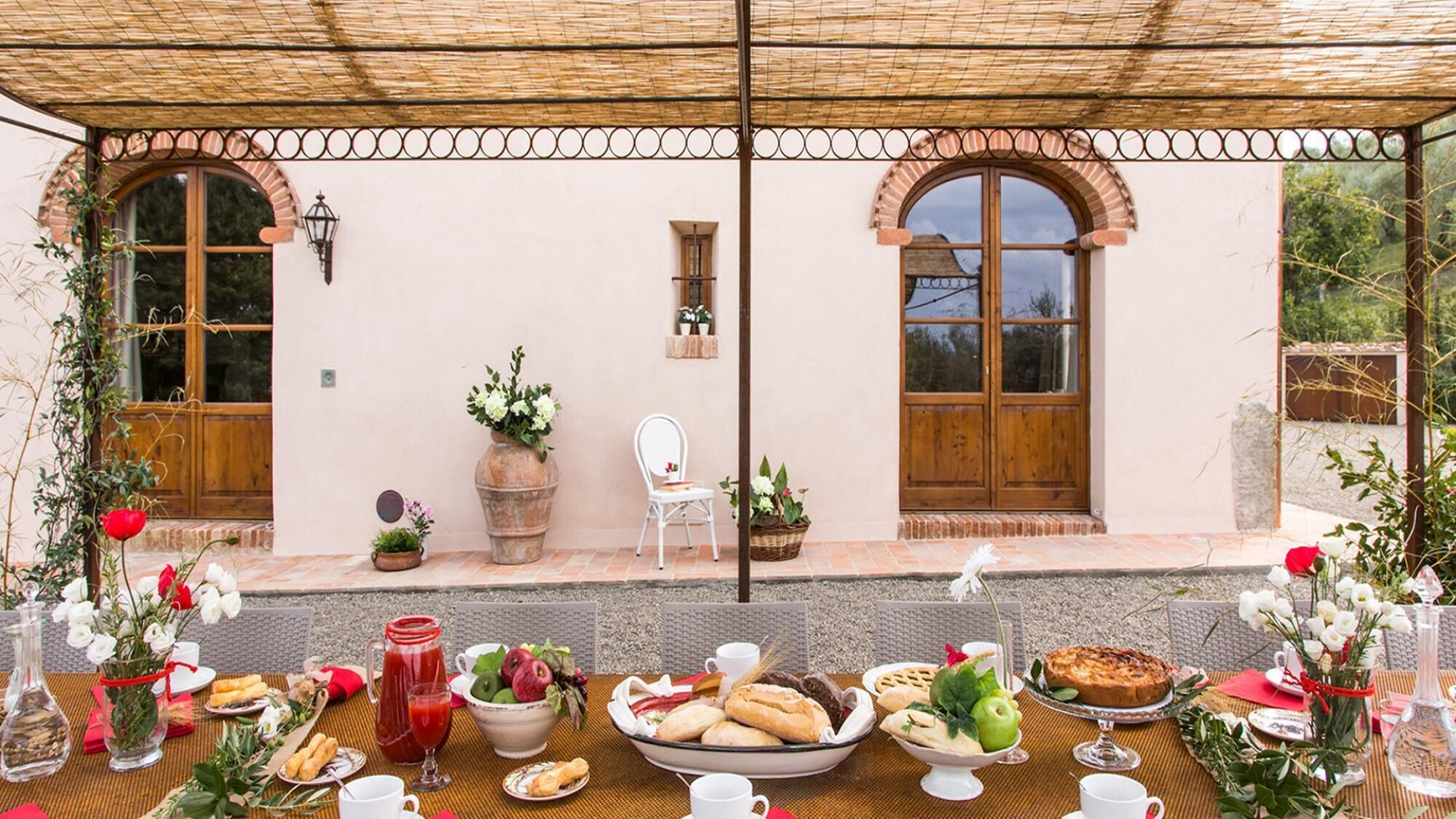 An outdoor dining area with a table set for a meal, featuring a variety of dishes and drinks.