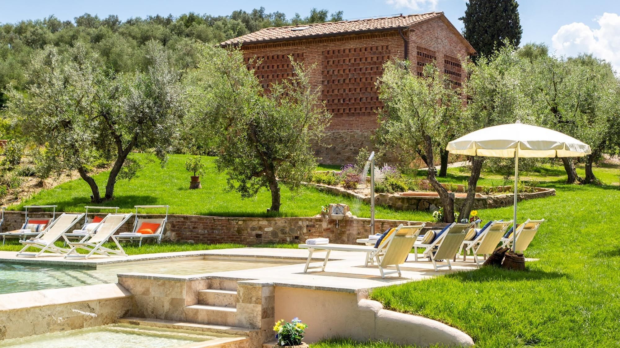 A pool area with lounge chairs, a stone wall, and a brick building in the background.