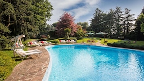 A swimming pool with lounge chairs and umbrellas, surrounded by trees and greenery. - Villa Pina 8 2 in Sulbiate (Sulbiate)