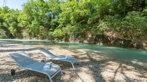Two sun loungers on a gravel path beside a clear river, surrounded by dense green trees and rocky cliffs. - Villa Monica 8 in Greti (Greve in Chianti)
