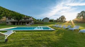 A pool area with lounge chairs, a stone building, and a grassy landscape. - Villa Monica 8 in Greti (Greve in Chianti)