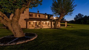 A stone villa with a patio, outdoor seating, and a well-maintained lawn at dusk. - Villa Monica 8 in Greti (Greve in Chianti)