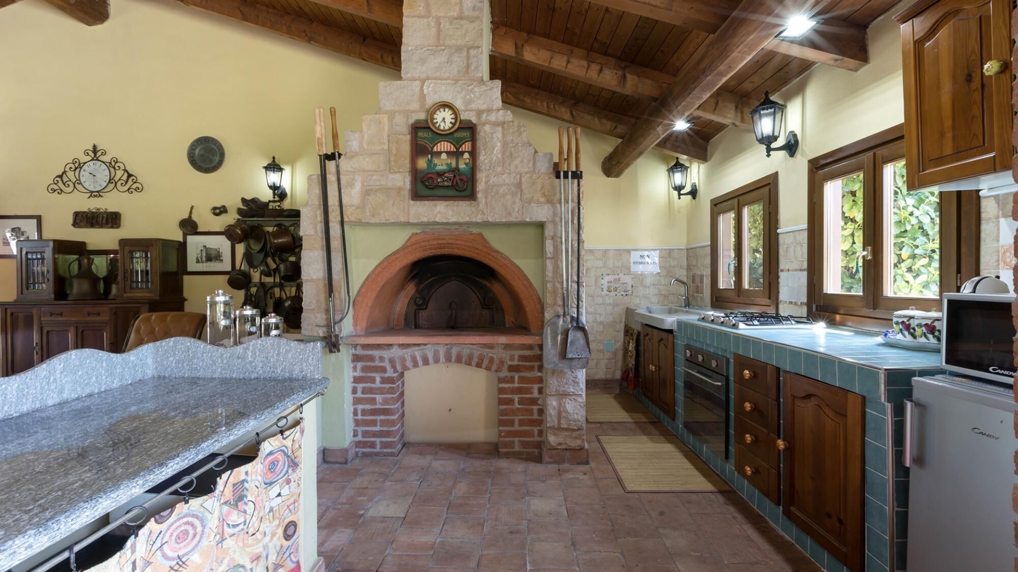 A kitchen with a brick oven, wooden cabinets, and a stone countertop.