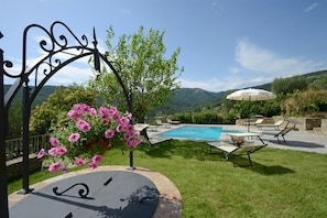Uma área na piscina com vista para montanhas, um pérgola com flores cor-de-rosa e espreguiçadeiras.