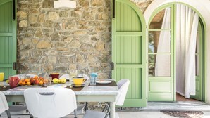 A stone wall with a table set for breakfast, green shutters, and a view through an arched window. - Villa Elsa 6 in La Vigna (Villafranca in Lunigiana)
