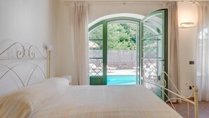 A bedroom with a bed, a window with a view of a swimming pool, and a door leading outside. - Villa Elsa 6 in La Vigna (Villafranca in Lunigiana)