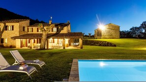 Une maison en pierre avec une piscine, un espace extérieur aménagé pour s’asseoir et une terrasse bien éclairée.