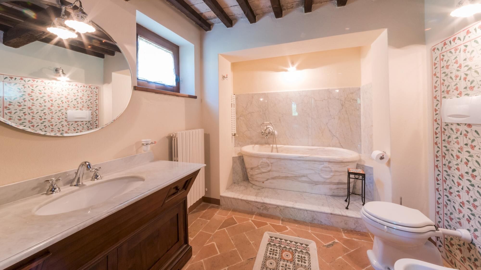 A bathroom with a marble bathtub, a double sink vanity, and a toilet.