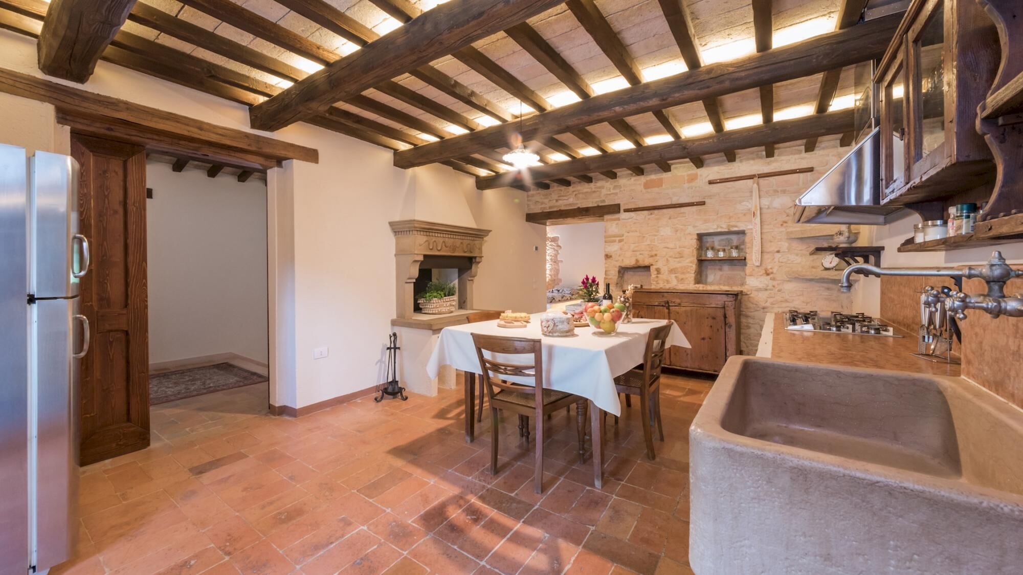 A rustic kitchen with exposed wooden beams, a stone fireplace, and a large sink.
