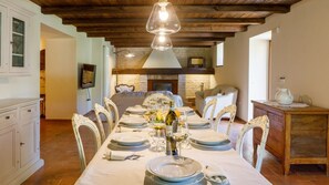 Comedor con una mesa larga dispuesta para seis comensales, chimenea y pared de piedra al fondo.