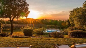 A pool area with lounge chairs, surrounded by well-maintained lawns and trees, with a sunset in the background. - La Cerqua 8 in Gualdo Cattaneo (Gualdo Cattaneo)