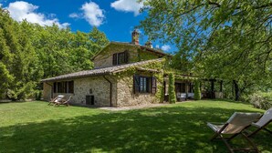 A stone house with a tiled roof, surrounded by a well-maintained lawn and trees. - La Cerqua 8 in Gualdo Cattaneo (Gualdo Cattaneo)