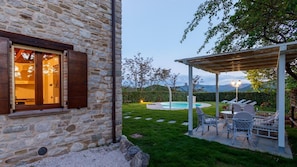 A stone building with a pool, outdoor seating, and a view of mountains.