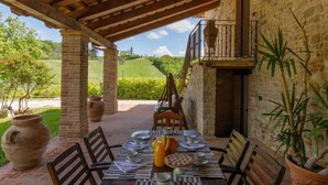An outdoor dining area with a brick table set for breakfast, surrounded by stone walls and potted plants. - Villa Agostini 10 in Ponte Doccia (Piandimeleto)