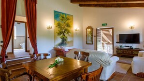 A dining area with a wooden table and chairs, a painting on the wall, and a television in the background. - Villa Agostini 10 in Ponte Doccia (Piandimeleto)