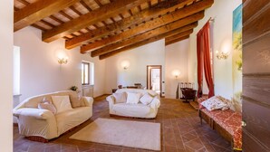 A spacious living room with high wooden ceilings, two white sofas, a red patterned bench, and a view of the adjacent room. - Villa Agostini 10 in Ponte Doccia (Piandimeleto)