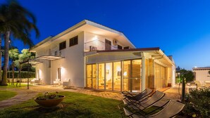 A modern house with a large glass door leading to a well-lit interior, a balcony, and a patio area with outdoor seating. - Villa D Aquino 8 2 in Casarano (Casarano)