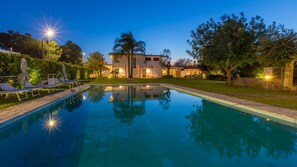Una piscina con sillas de descanso y una casa iluminada al fondo.
