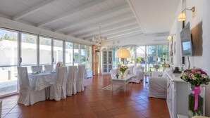 A spacious room with large windows, a dining area with tables and chairs, a sofa, and a TV mounted on the wall. - Villa D Aquino 8 2 in Casarano (Casarano)