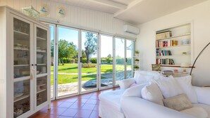 A spacious living room with a white sofa, a bookshelf, and a sliding glass door leading to a garden. - Villa D Aquino 8 2 in Casarano (Casarano)