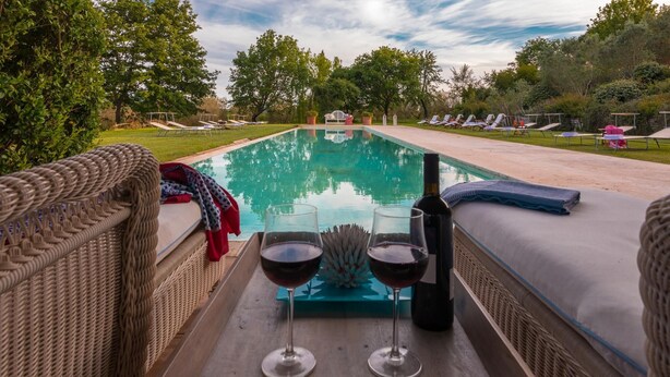 A poolside view with lounge chairs, a wicker sofa, and a table with wine glasses and a bottle. - Quercia Felice 17 in Manciano (Manciano)