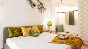 Quarto moderno com cama, almofadas, mesa de cabeceira, planta e porta-toalhas.