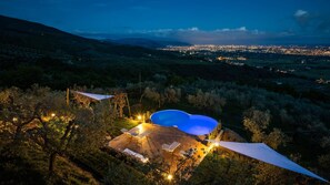 Piscina rodeada por área ajardinada, com vista para o horizonte urbano ao entardecer.