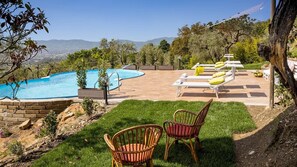 A backyard with a swimming pool, lounge chairs, and a grassy area with wicker chairs.