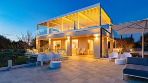 A modern two-story house with a glass facade, outdoor seating area, and a well-lit patio. - La Perla tra gli Ulivi 12 (San Vincenzo)