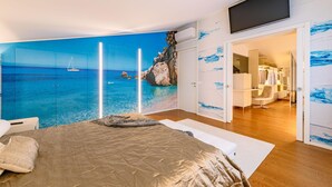 A bedroom with a large bed, a TV mounted on the wall, and a view of the sea through a glass door. - La Perla tra gli Ulivi 12 (San Vincenzo)