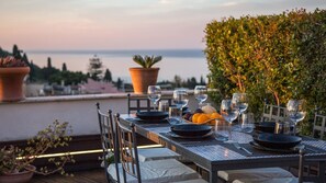 An outdoor dining table set with plates, glasses, and a fruit basket, overlooking a body of water.