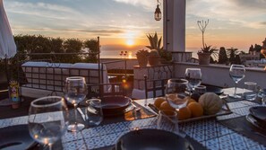 A sunset view from a terrace with a table set for dining, glasses, and potted plants.