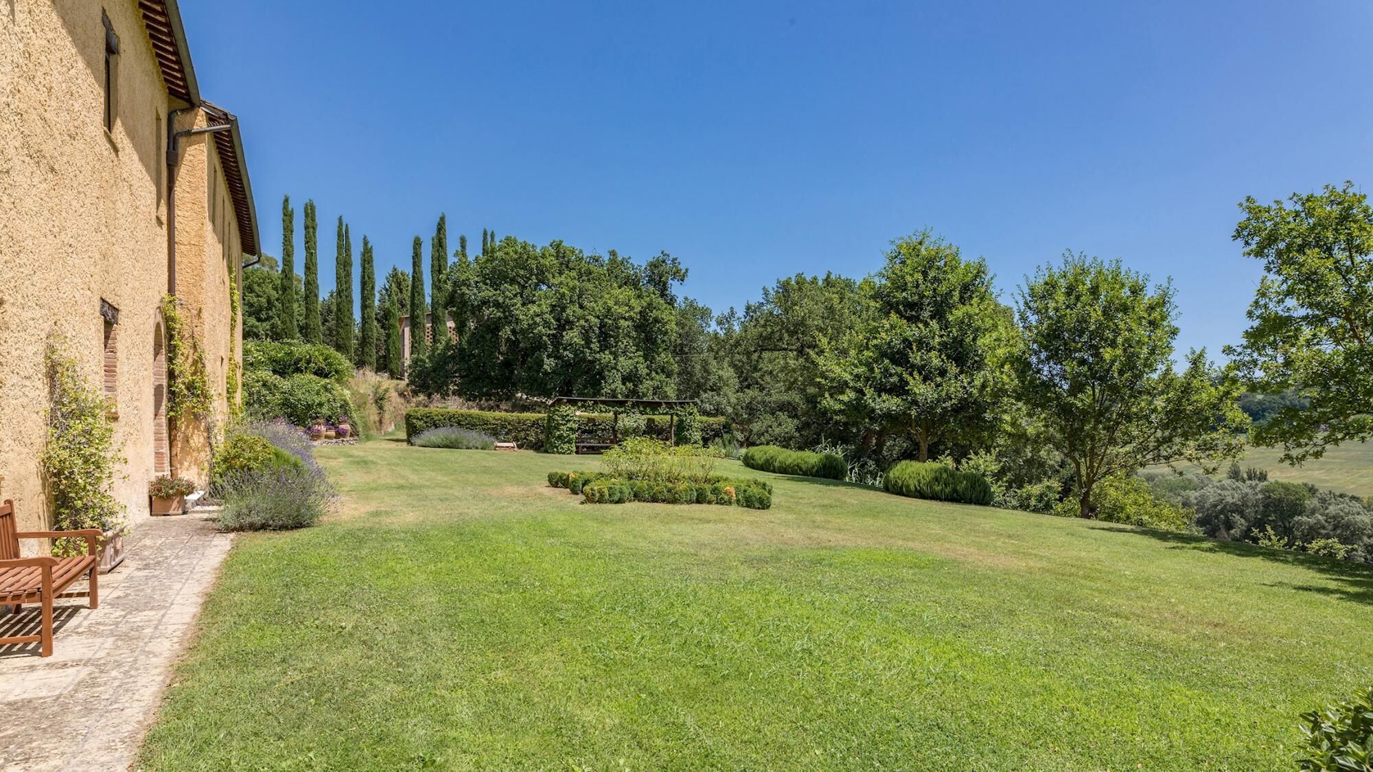 Un jardin bien entretenu, agrémenté d’un bâtiment en pierre, d’un banc en bois et d’une pergola.