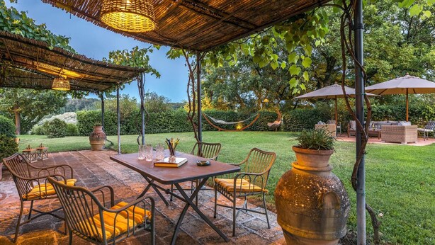 Um pátio externo com mesa e cadeiras, rodeado por vegetação e uma rede.