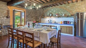 A rustic dining area with a stone arch and wooden beams, a kitchen with modern appliances, and a view through an open door. - Casale del Viaggiatore 10 (San Casciano dei Bagni)
