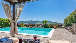A pool area with lounge chairs, a table with drinks, and a view of hills. - Casale del Viaggiatore 10 (San Casciano dei Bagni)