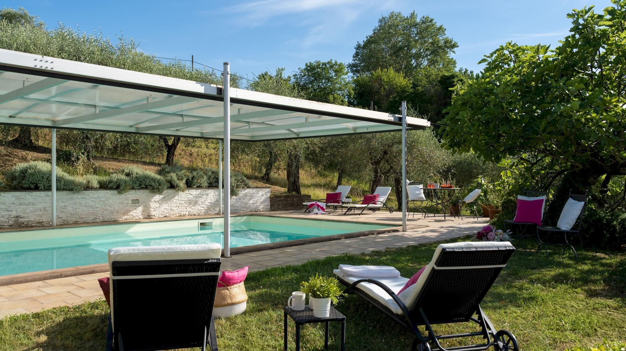 Zona de piscina con cerramiento de vidrio, sillas de descanso y una pequeña mesa con una planta.