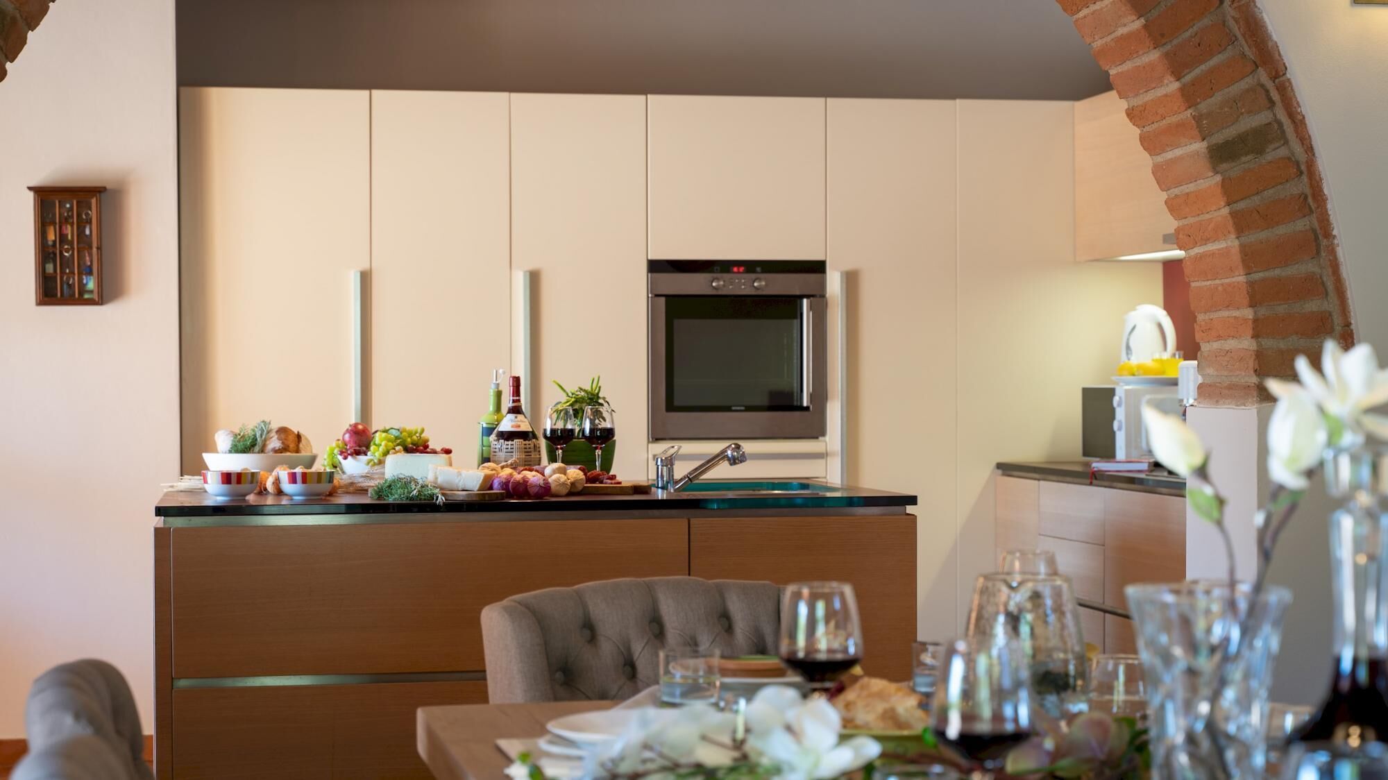 Een moderne keuken met een inbouwoven, een eethoek met een tafel gedekt voor twee personen, en een bakstenen boog.