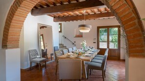 A dining area with a long table set for a meal, a staircase, and a view of greenery outside.