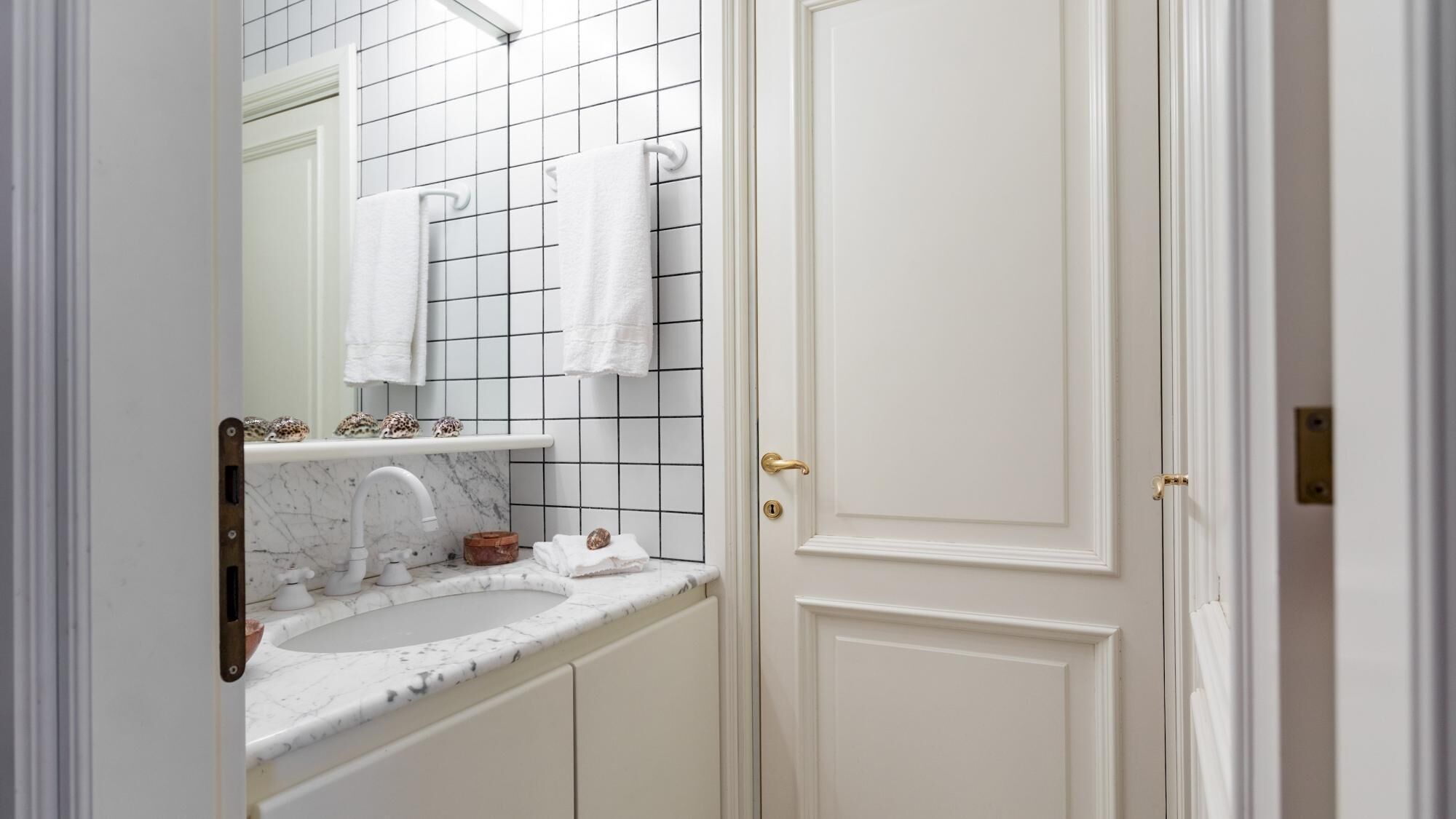 A bathroom with a white sink, a mirror, and a door with a gold handle.