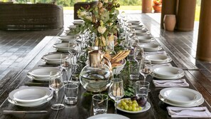 Une longue table à manger, dressée pour un repas, avec des assiettes, des verres et un centre de table composé de fleurs et de pain.
