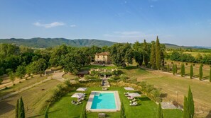 Une villa avec piscine, entourée d’un jardin bien entretenu et de grands arbres.