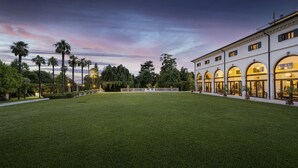 Un pati espaiós amb un jardí ben cuidat, envoltat d'un edifici clàssic amb finestres d'arc i una bandera a la part superior.