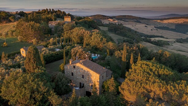 A stone building surrounded by trees and fields, with a small tower and a swimming pool visible. - Podere Orcio 10 in Volterra (Volterra)