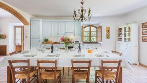 A dining room with a large table set for six, light blue cabinets, a chandelier, and a view through a window. - Podere Orcio 10 in Volterra (Volterra)