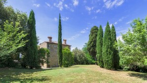 A stone building with a tiled roof, surrounded by tall cypress trees and a grassy lawn. - Podere Orcio 10 in Volterra (Volterra)