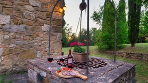 A stone wall with a rustic outdoor seating area featuring a table with a bottle of wine, glasses, and a wooden board with food. - Podere Orcio 10 in Volterra (Volterra)
