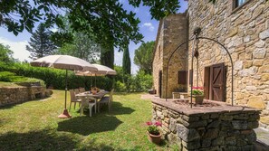 An outdoor patio with stone walls, a table with chairs, and a large umbrella. - Podere Orcio 10 in Volterra (Volterra)