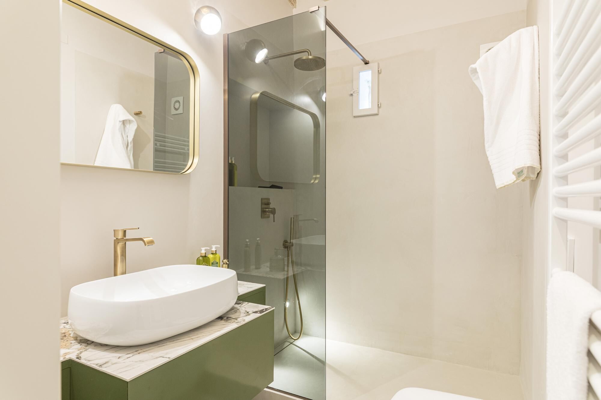 A modern bathroom with a large white sink, a glass-enclosed shower, and a mirror with a gold frame.