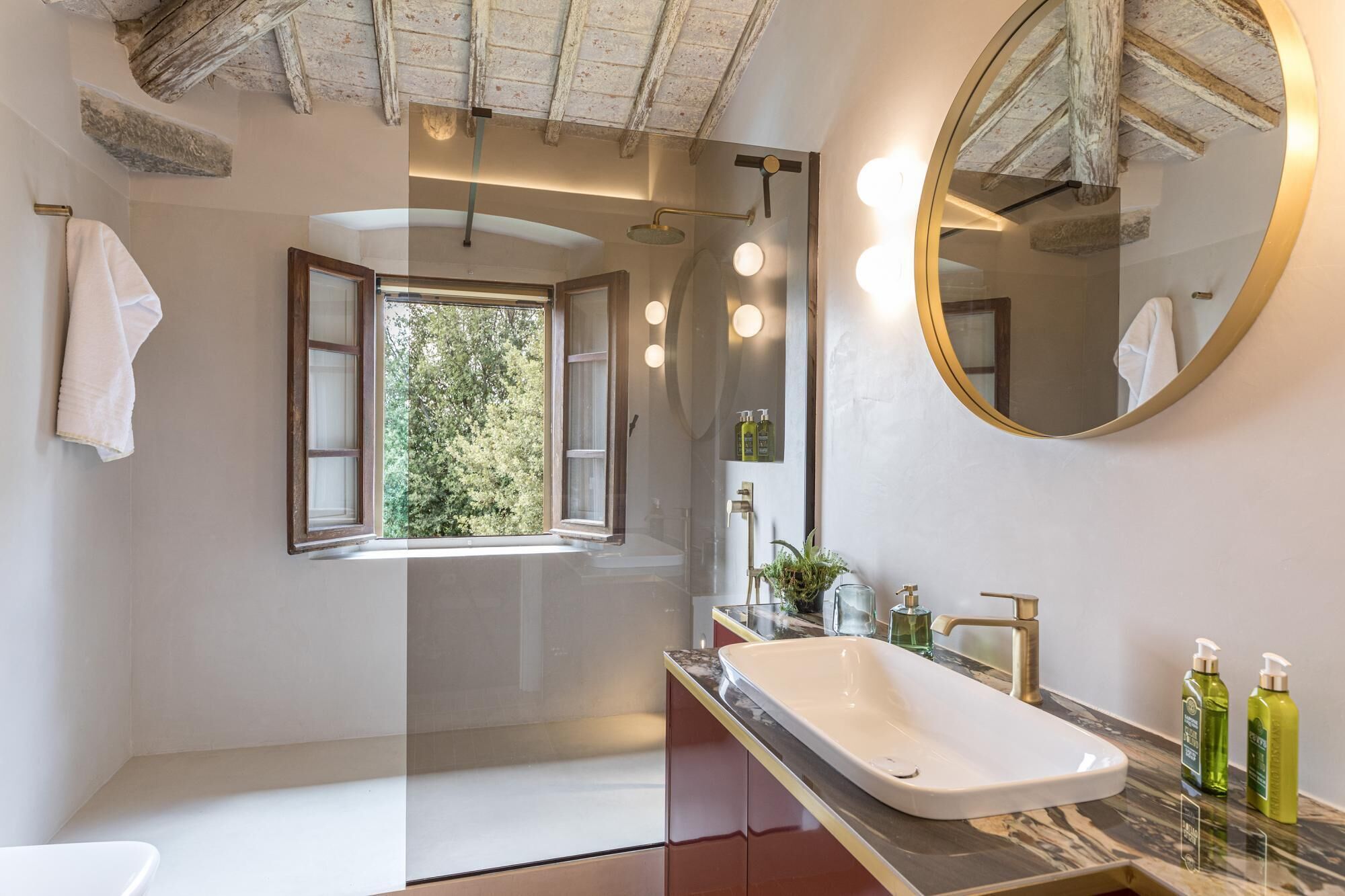A modern bathroom with a large window, a freestanding bathtub, a vanity with a sink, and a round mirror.